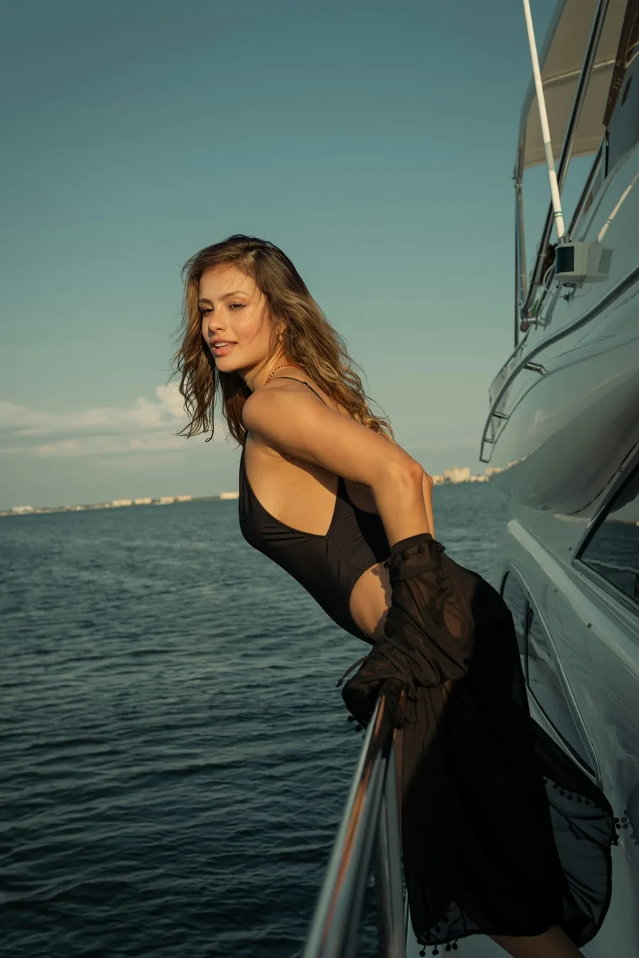 Model in black swimwear and a sheer resort layer aboard a luxury yacht